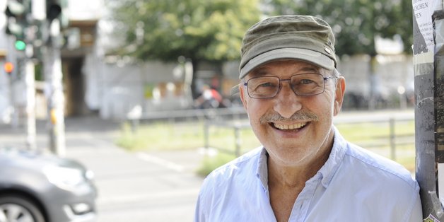 © BAGSO/Dietl Ein älterer Mann mit einer grünen Schirmmütze lehnt an einer Straßenlaterne und lacht in die Kamera