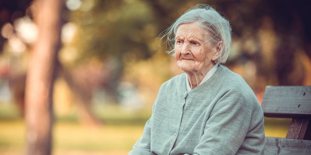 ©Andrey Bandurenko_stock.adobe.com Eine alte Frau sitzt auf einer Bank im Park. Sie schaut sehr traurig