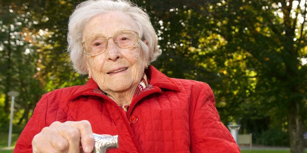 © Peter Maszlen_adobe.stock.com Alte Frau mit Stock sitzt auf einer Bank.